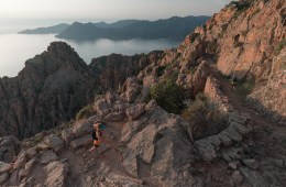 Two runners jogging across a trail at the edge of the mountains.