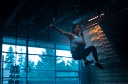 Alannah Yip training on rings inside a dark climbing gym backlit by blue lighting.