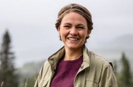Christiane Dolva smiles for the camera with evergreen trees in the background.