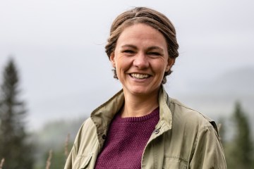 Christiane Dolva smiles for the camera with evergreen trees in the background.