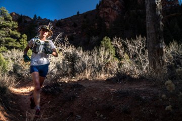 Clare Gallagher is running on a trail with mountains and blue sky behind her.