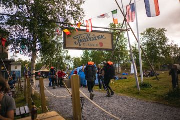 Two hikers have their back to the camera as they walk underneath a Fjallraven Classic sign.