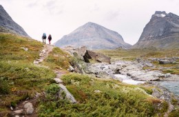 Two people hiking up a hill with mountains in the background.