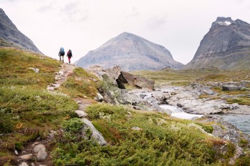 Two people hiking up a hill with mountains in the background.