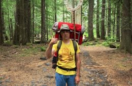 Tom Putnam stands in the woods with a big red backpack that had a butterfly net sticking out of it.