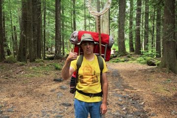 Tom Putnam stands in the woods with a big red backpack that had a butterfly net sticking out of it.