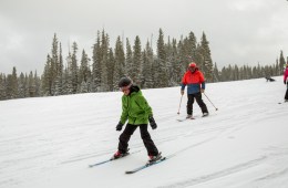 A young skier skis ahead of two adults at a ski resort