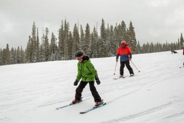 A young skier skis ahead of two adults at a ski resort