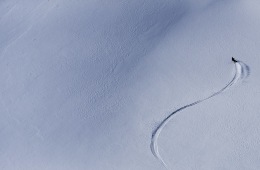 Michelle Parker captured from an aerial camera skiing down a mountain. She is a tiny bright spot in a sea of white.