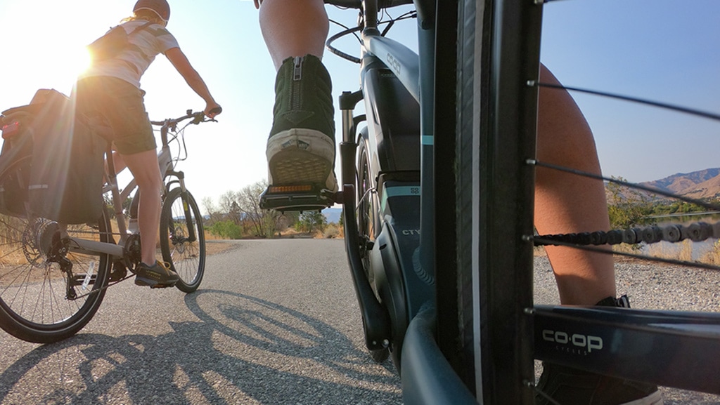 Two e-bikes seen pedaling away on an asphalt road