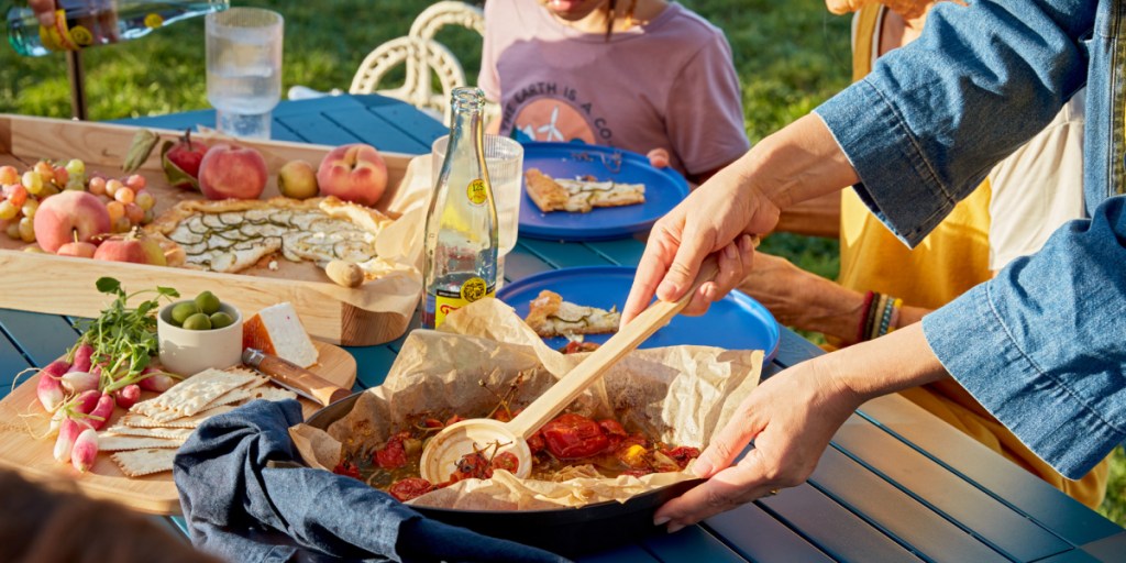A person scoops up some roasted cherry tomatoes with a wooden spoon