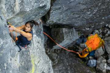 Alannah Yip climbing an outside rock climbing wall. She's wearing a black tank top as she reaches up for a hold.