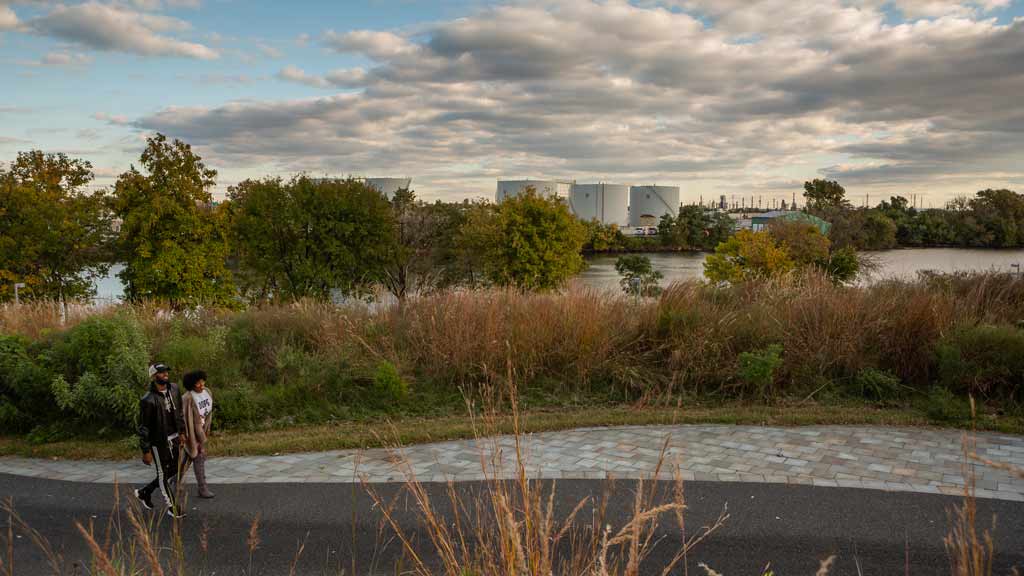 Two people walking on a paved trail along a river with expansive sky in the backdrop.