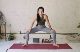 Yoga teacher Elena Cheung is in a horse stance on a red yoga mat smiling at the camera.