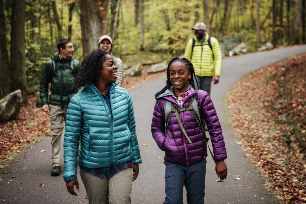 a family dressed in brightly colored puffy jackets walks on a paved path in the forest