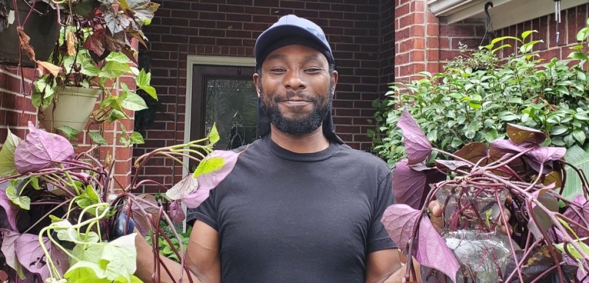 Marcus Bridgewater is smiling at the camera while holding plants in both of his hands.