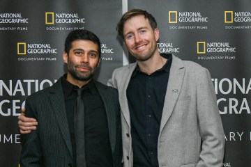 Max Lowe smiles at the camera with his arms around another man. The backdrop says National Geographic Documentary Films.