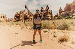 Miranda is holding hiking poles with her arms outstretched smiling into the camera. There are rock formations behind her.