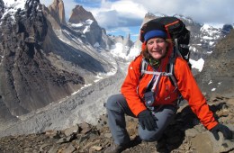 Laurie Watt posing at the top of a mountain in a red coat and backpack