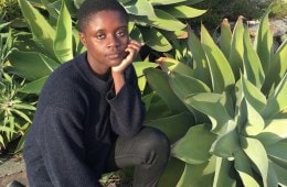 A woman in a navy sweater and black jeans kneels in front of a group large aloe plants.