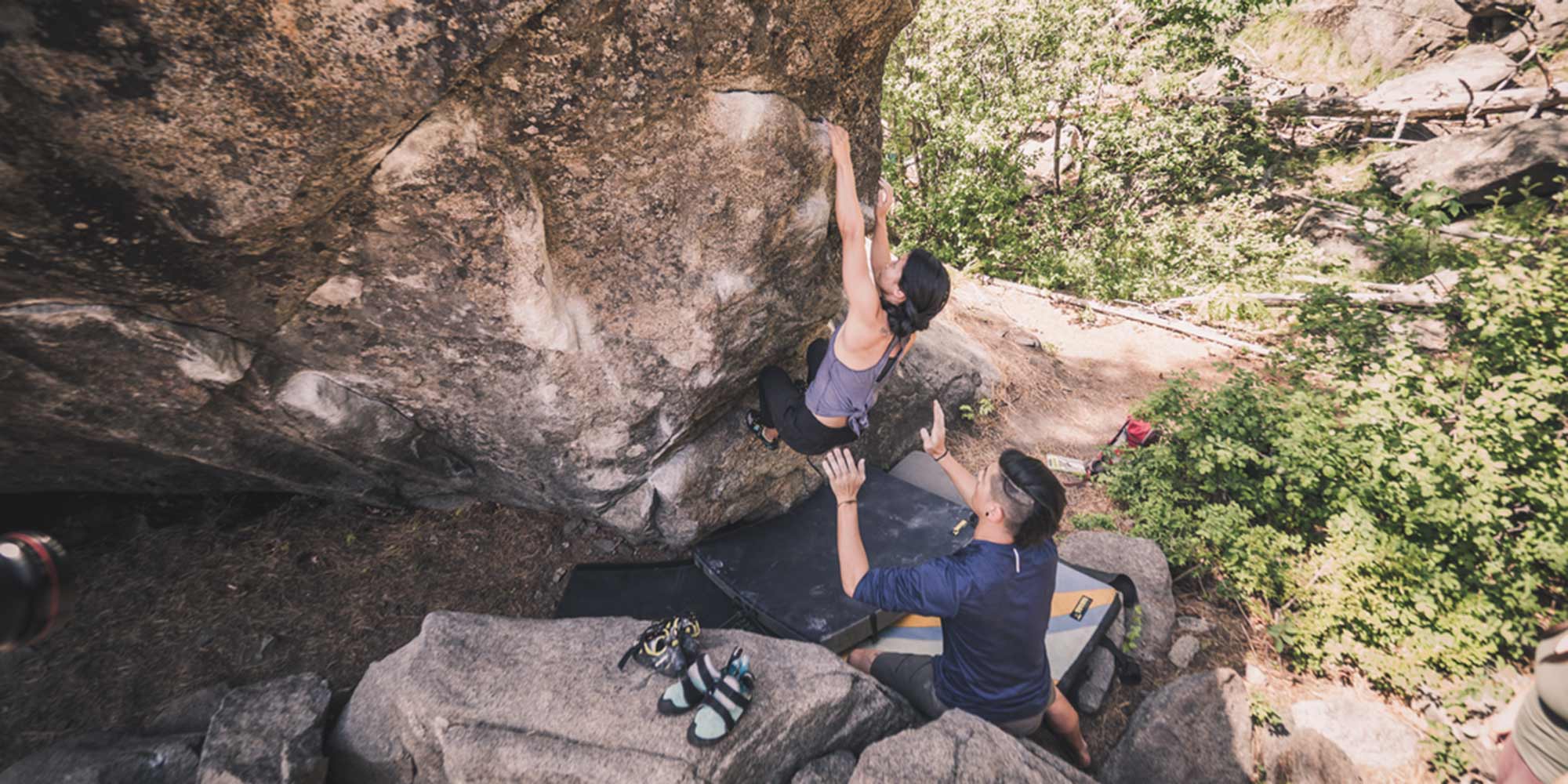 A person assists another who is climbing on a boulder.