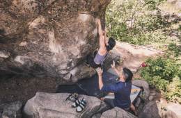 A person assists another who is climbing on a boulder.