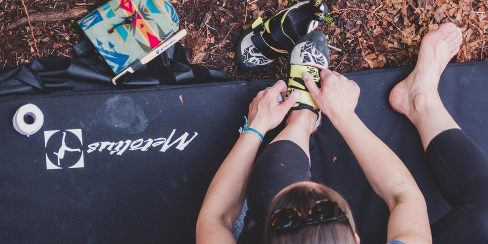 Climber sitting on a crash pad putting climbing shoes on.