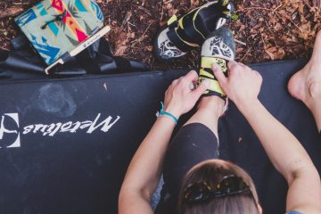 Climber sitting on a crash pad putting climbing shoes on.