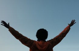 A Black person reaching their arms into the sky