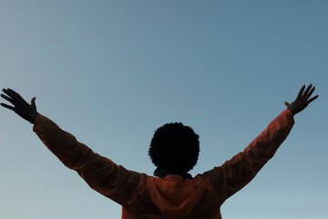 A Black person reaching their arms into the sky