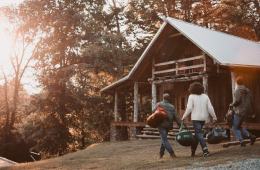 three people walking to a log cabin surrounded by trees in autumn setting