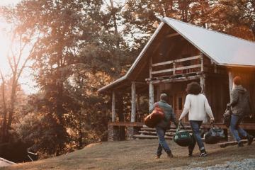 three people walking to a log cabin surrounded by trees in autumn setting