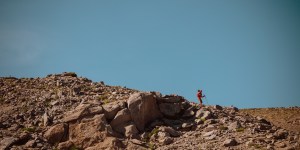 A man wearing a red jacket and using trekking poles runs down rocky mountain terrain in Washington State