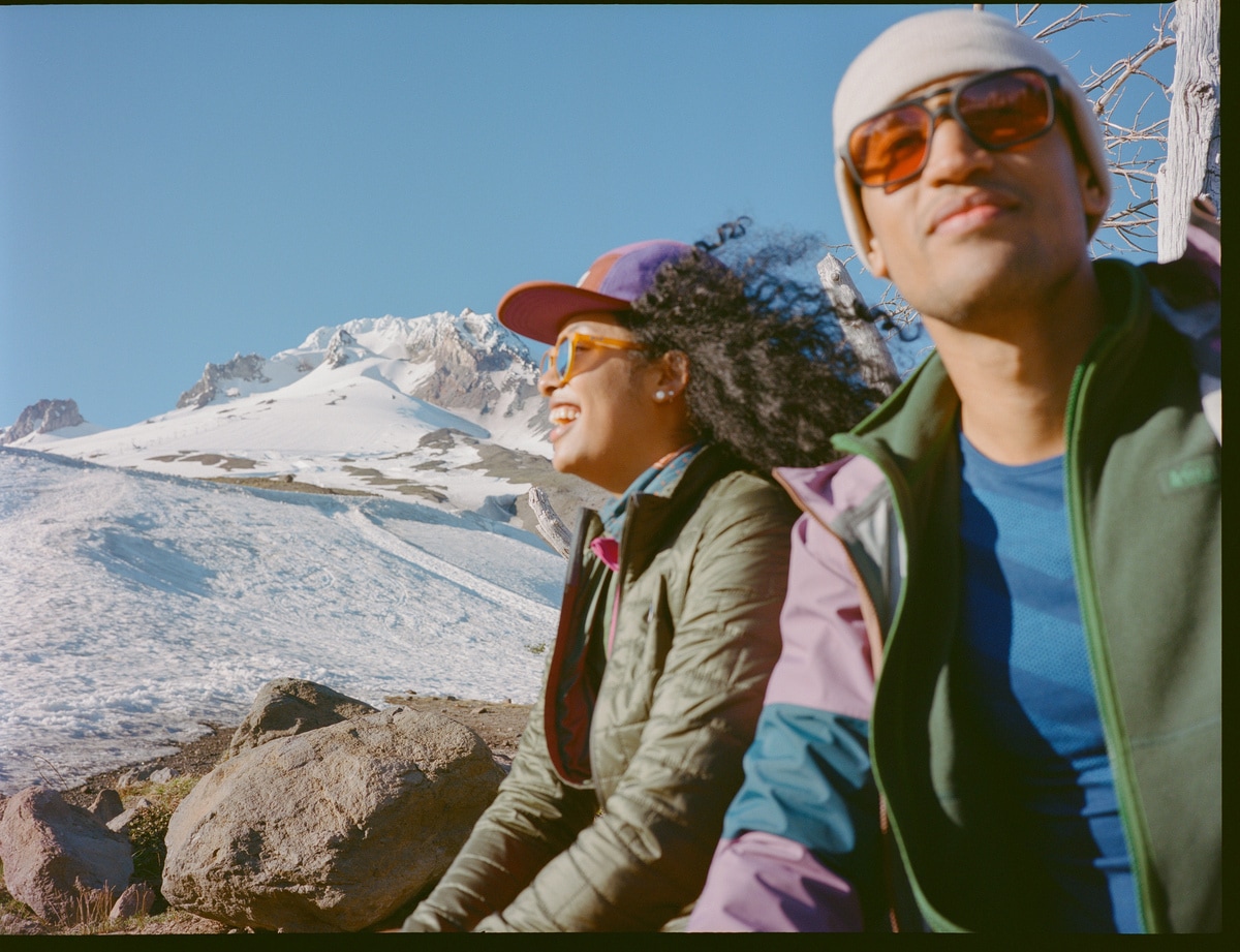 Two people wearing jackets in front of a snowy mountain backdrop