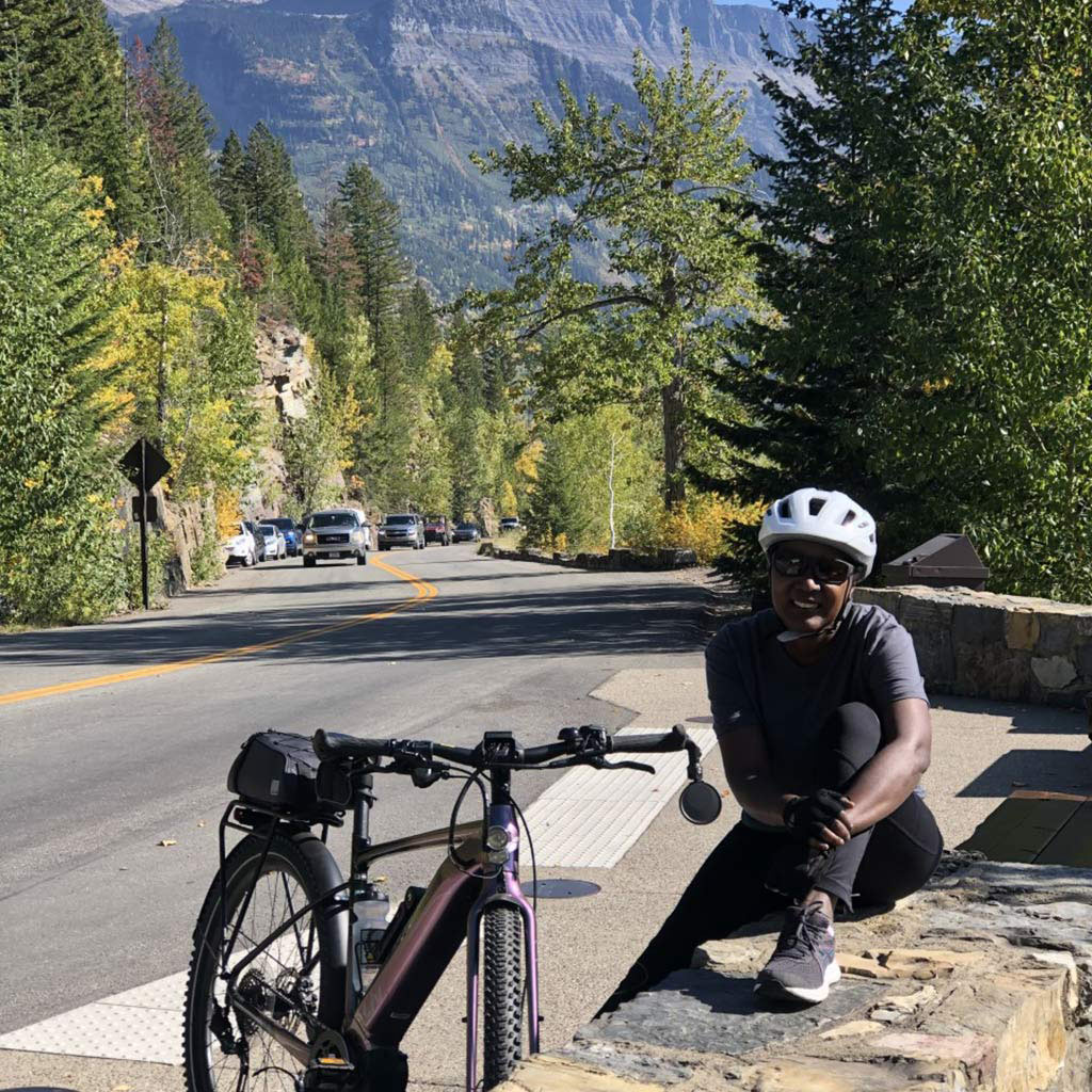 Person resting next to a bike along a scenic road in Glacier National Park