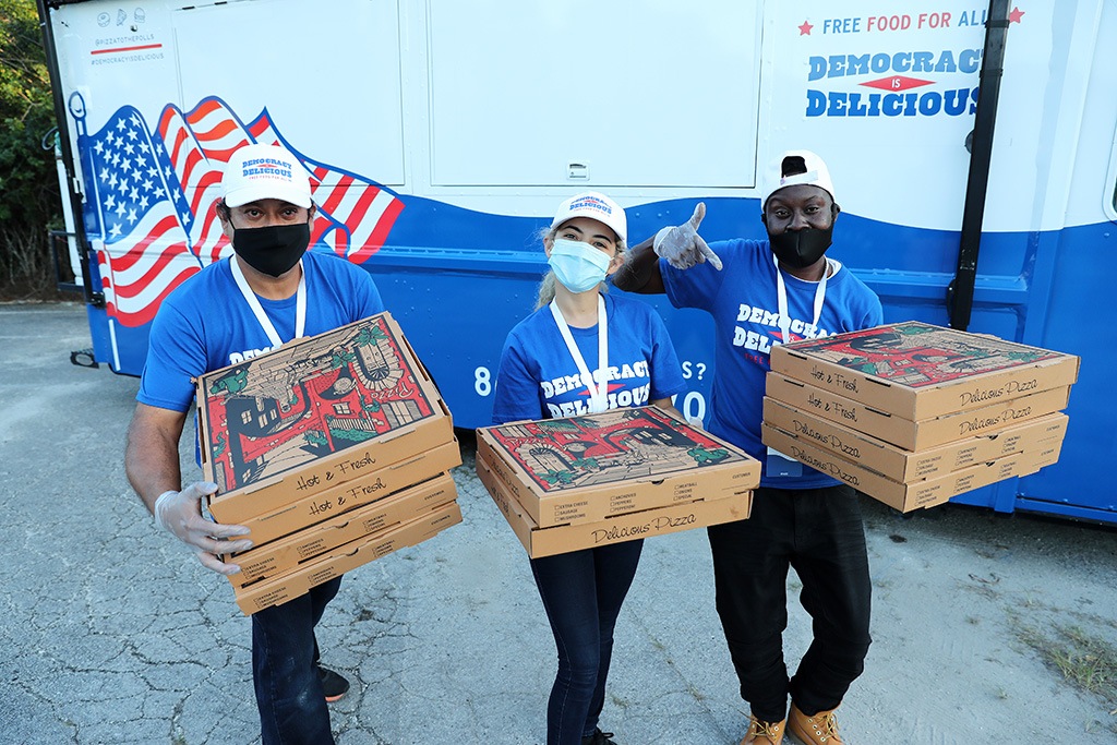 Three volunteers hand out pizza to voters waiting in line