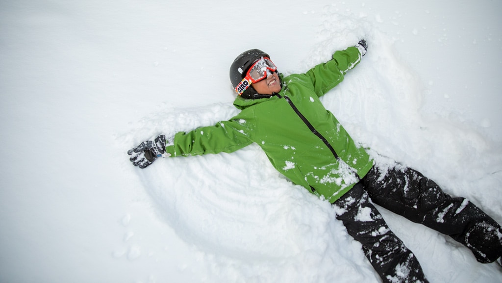 A young person lying down in the snow with arms widespread making a snow angel.