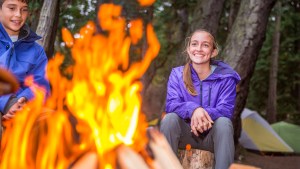 Two young people sit smiling around a camp fire