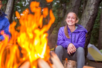 Two young people sit smiling around a camp fire