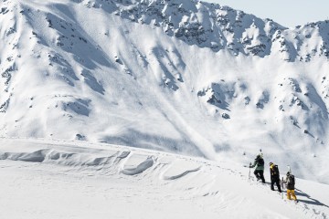 Three skiers walk along a snowy ridge.