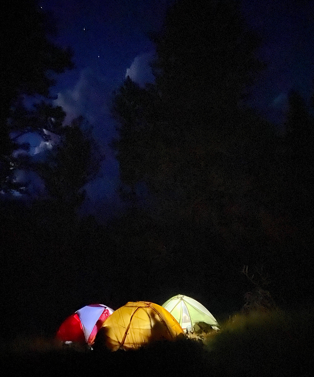 Three tents are lit up against a pitch-dark night sky