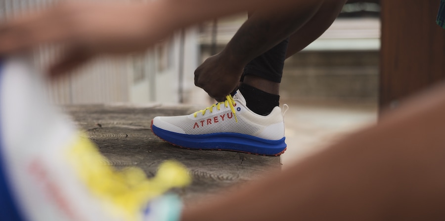 A person, with their foot up on a bench, ties their Atreyu Daily Trainer road running shoe. 