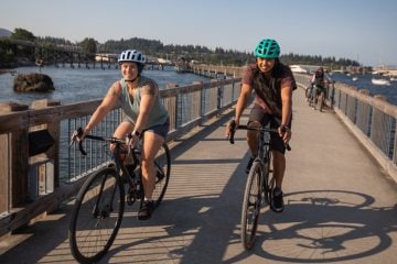 Two people biking along a boardwalk over water.