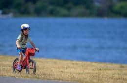 A child rides a bike along a body of water.
