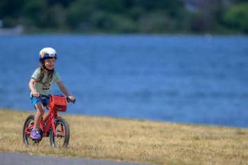 A child rides a bike along a body of water.
