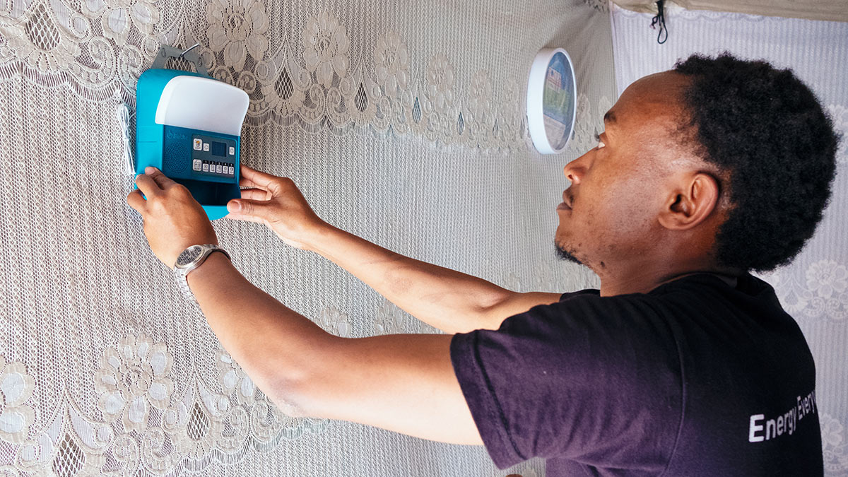 A person hangs a small solar power unit on the wall.