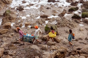 Four people walk along what looks like a rocky shoreline.