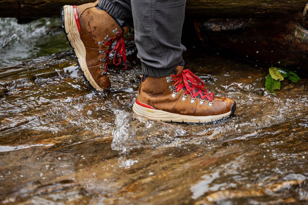 A person wearing boots steps on rocks covered by water.