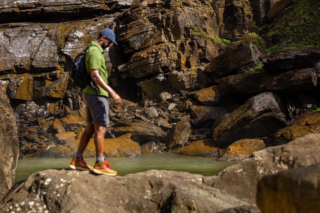 A person wearing hiking boots stands on a rock next to water.