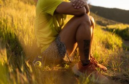 A person sitting on a grassy hill in a pair of red REI Co-op Swiftland MT Trail-Running Shoes.